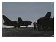 Military personnel stand near planes on an aircraft carrier.