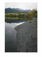 Mountains Cast Reflections into Clear Water Along a Pebbly Shore