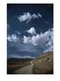 Dirt road to ranch through desert hills against a blue cloudy sky