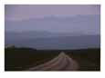 Twilight view of road leading to fog-shrouded mountains.