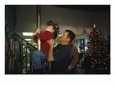 With a Lighted Christmas Tree in the Background, a Firefighter Assists a Small Boy
