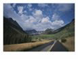 A Road Leads Through a Mountain Field with Mountains All Around